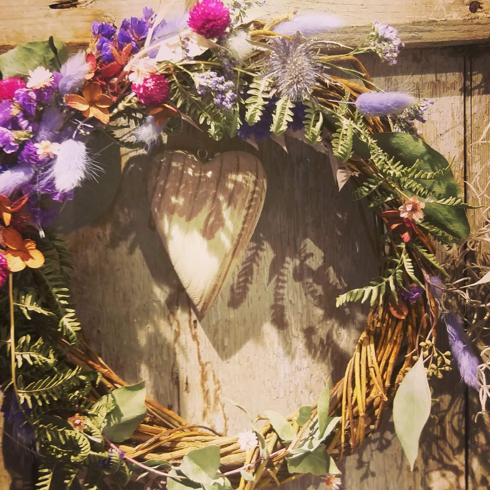 Couronne de fleurs et de graminées autour d’un cœur en bois